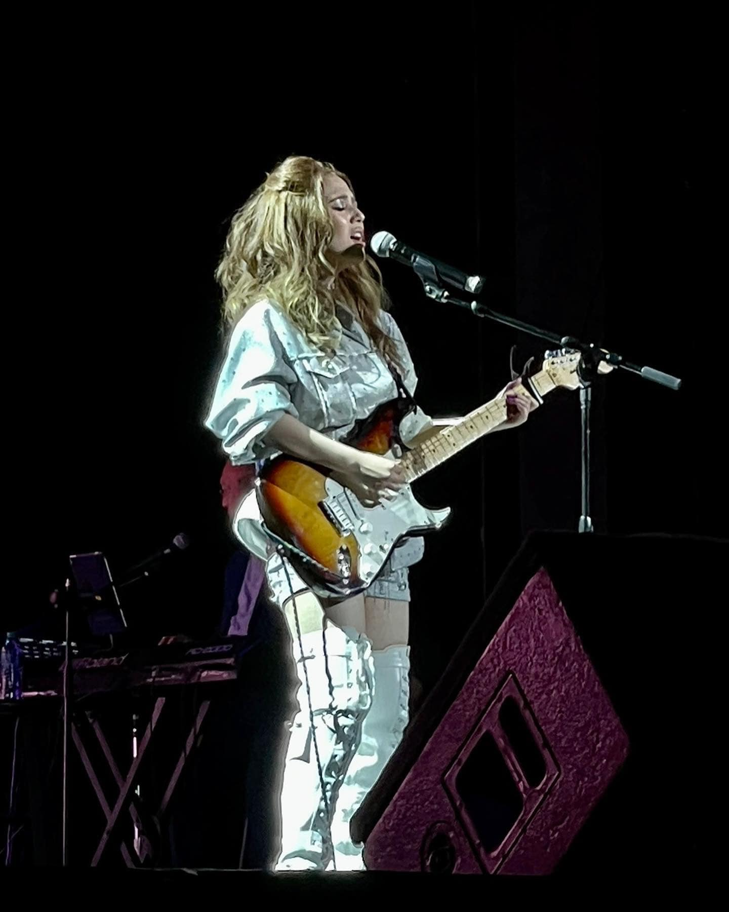 A person playing guitar on a stageDescription automatically generated with medium confidence